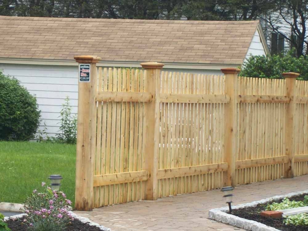 Wooden slat fence and matching gate beside a house with garden beds and paved walkway