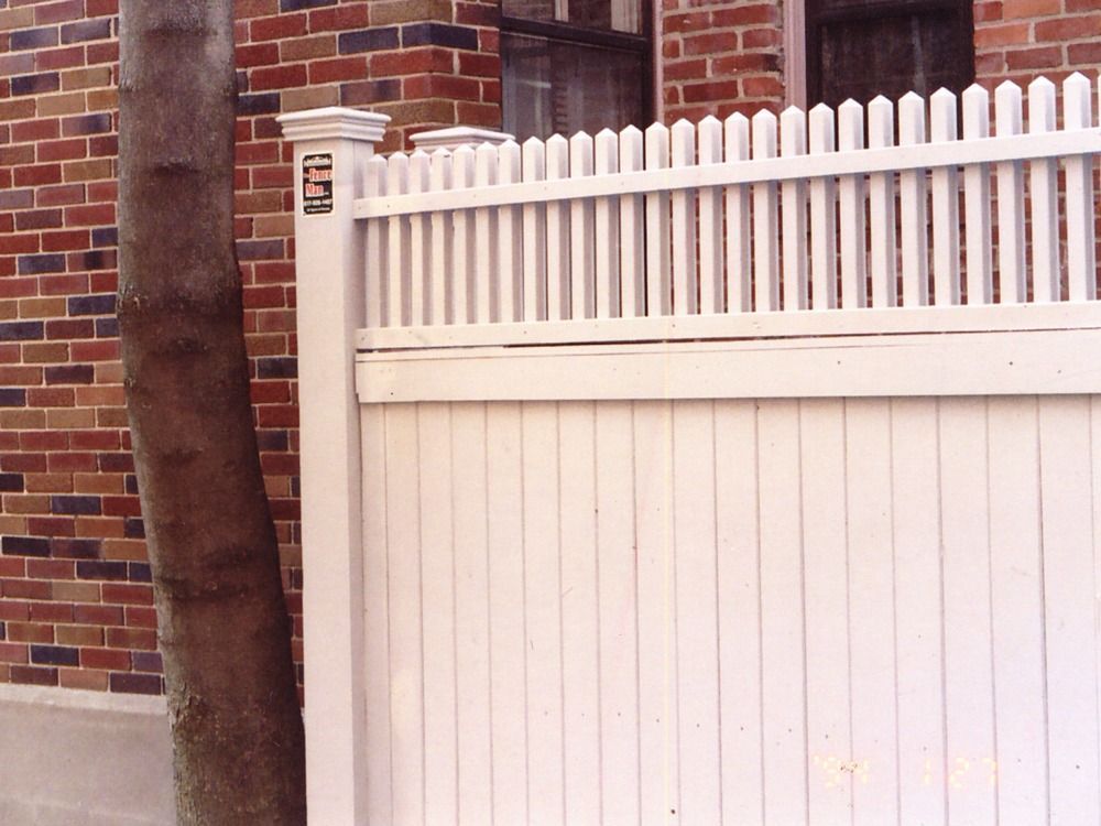 White picket fence beside a brick wall and tree trunk outdoors