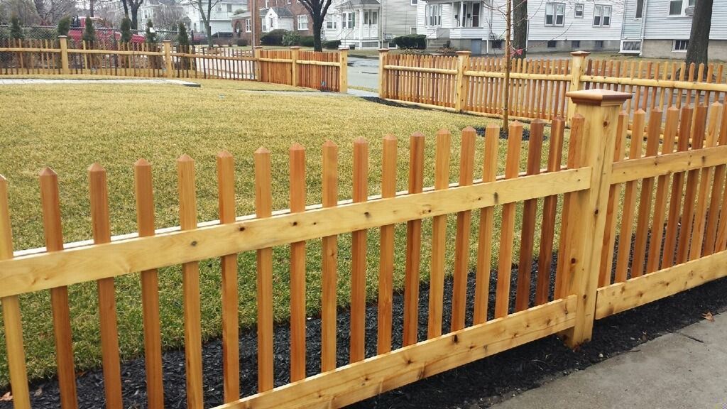 Wooden picket fence surrounding a grassy area along a paved path in a park