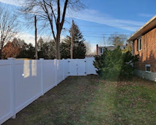 Backyard with white vinyl fence, brick house, bare trees, and patchy grass under a blue sky