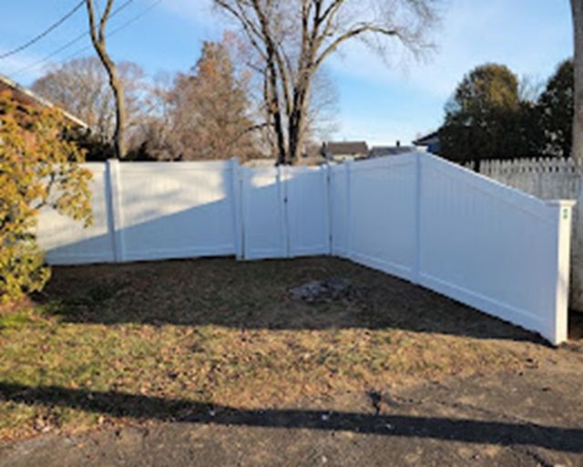 White vinyl fence panels around a bare yard under a clear blue sky
