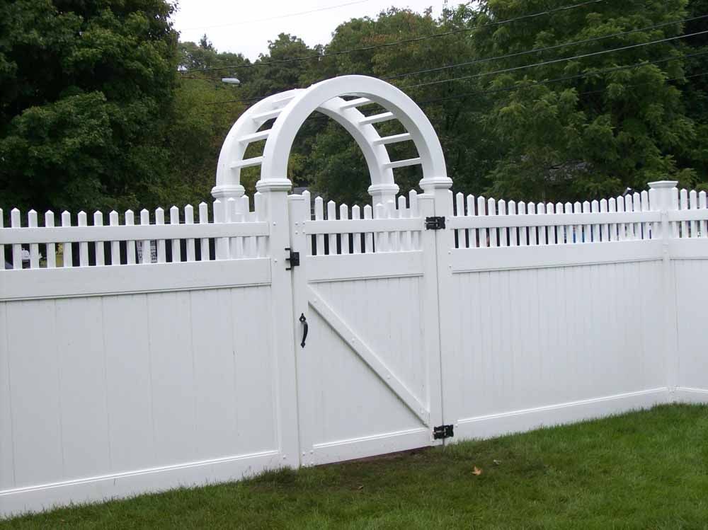 White picket fence with a central gate and arched trellis in a grassy yard