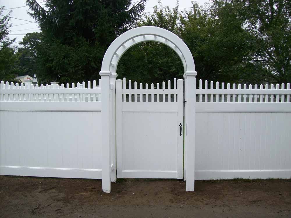 White fence with arched gate and arbor in front of trees