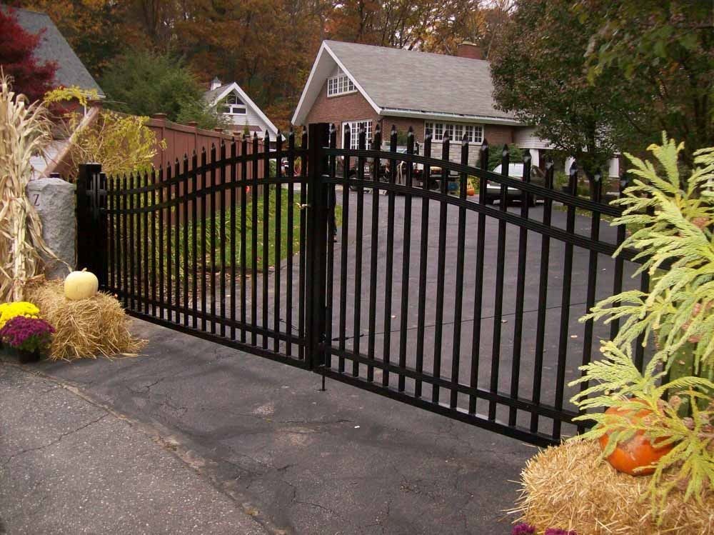 Black metal driveway gate in a landscaped residential entrance with autumn foliage.