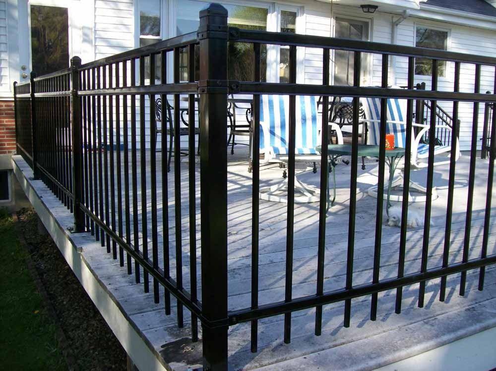 Black metal fence around a sunlit outdoor patio with tables and chairs