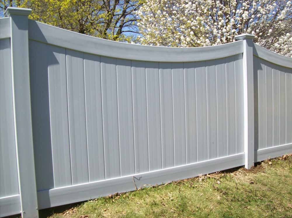 Light gray vinyl fence with curved top panels along a grassy yard under trees