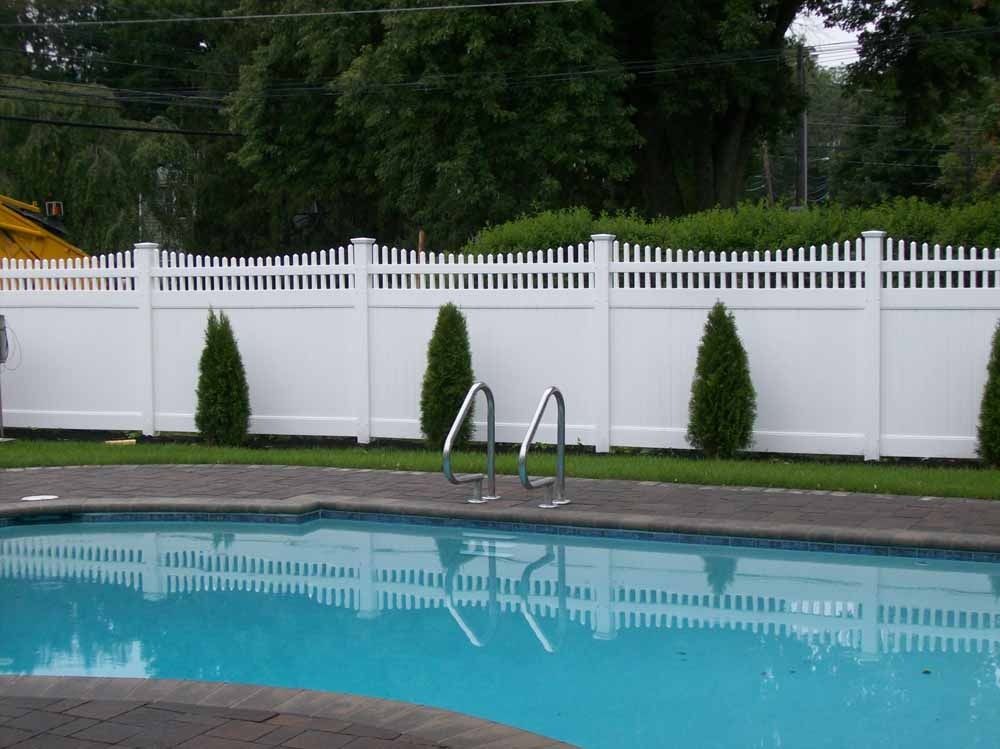 Backyard swimming pool with white fence and small evergreen shrubs along the edge