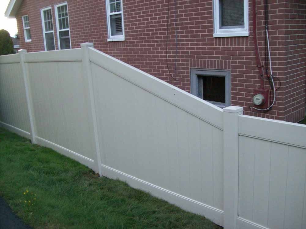 White vinyl fence with a sloped top in a grassy yard beside a brick house
