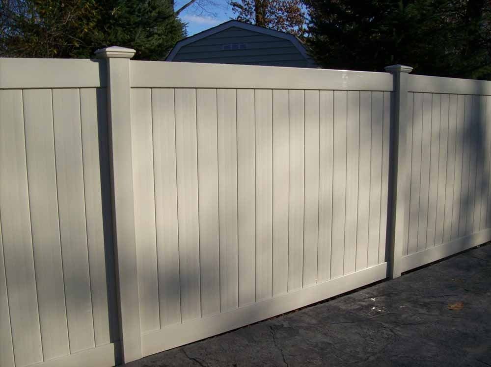 Light beige vinyl privacy fence with shadows along a driveway