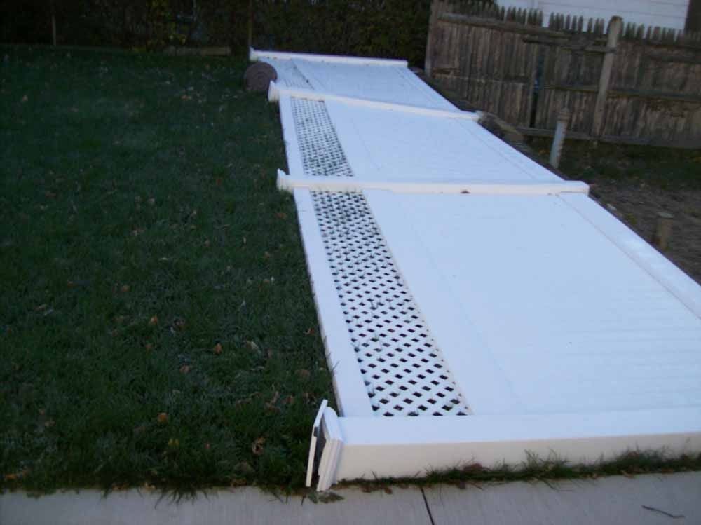 White outdoor privacy fence panels lying collapsed on grass beside a wooden fence.