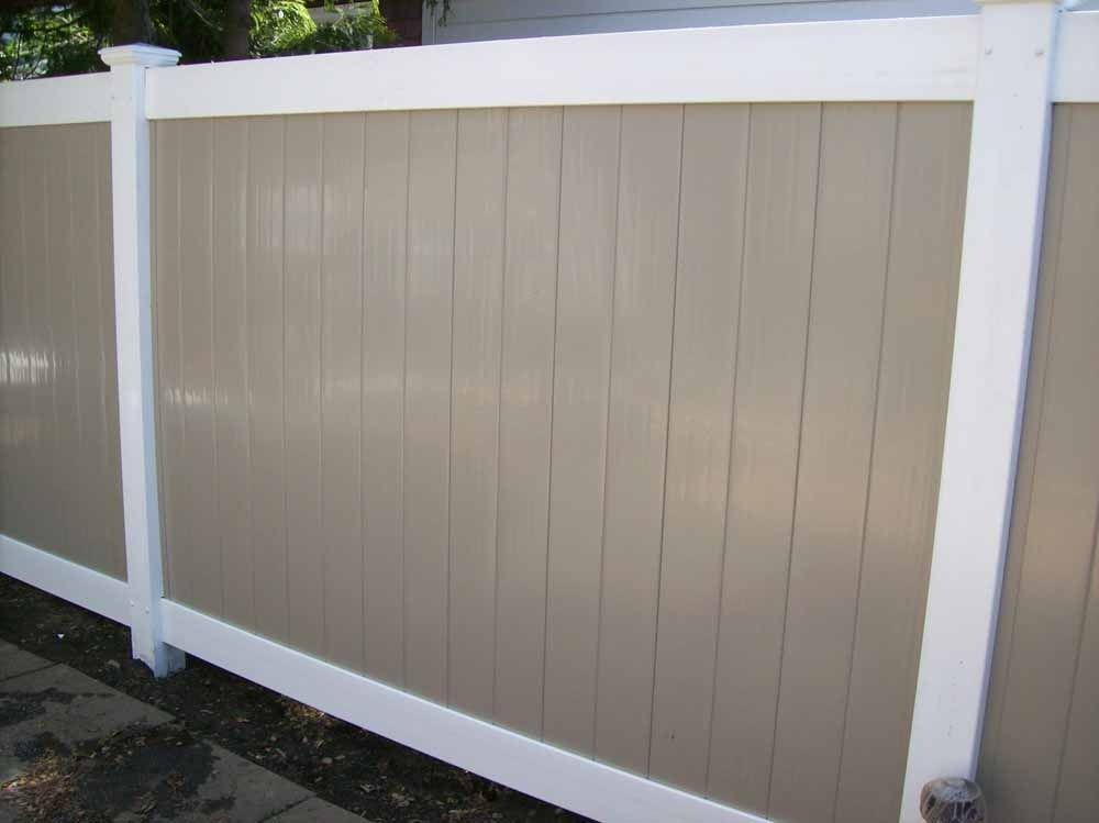 Beige vinyl fence panel with white posts and rails along a paved driveway