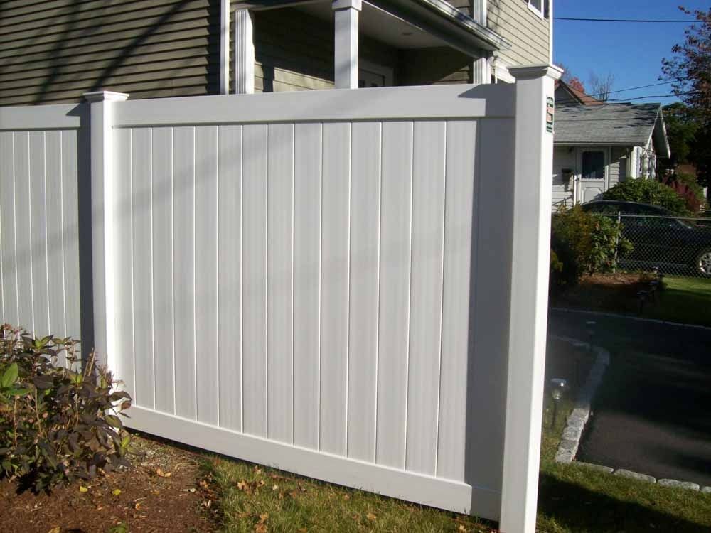 White vinyl privacy fence beside a house with a small garden and driveway entrance