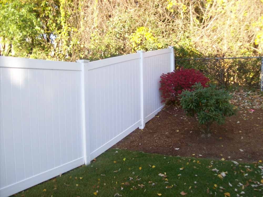White vinyl fence beside a yard with red and green shrubs under trees