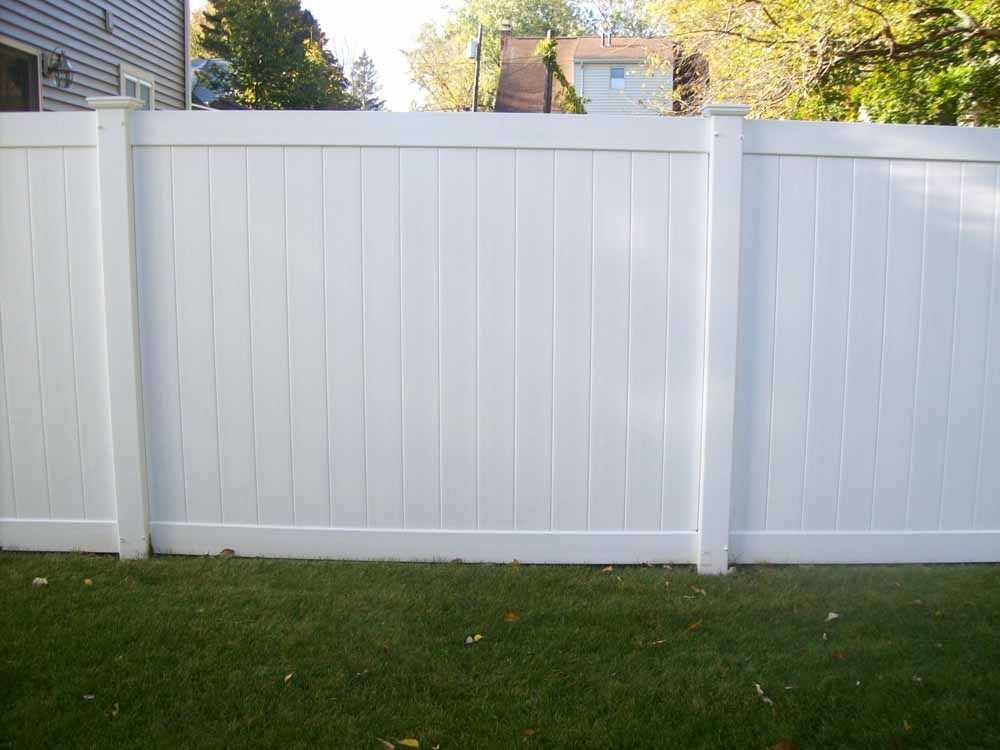 White vinyl privacy fence with green lawn in front and houses visible behind it