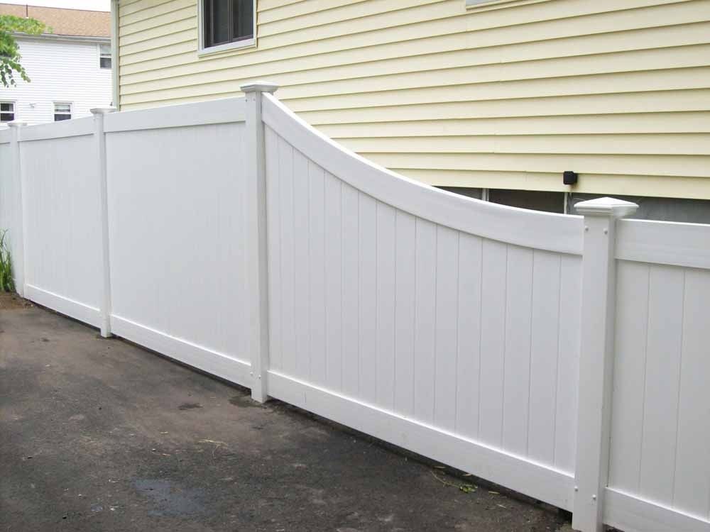 White vinyl fence with a curved top along a driveway beside a beige house