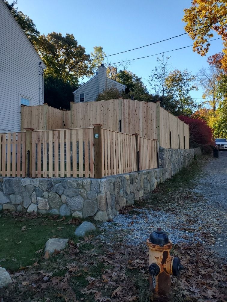 Wooden fenced stone retaining wall beside a gravel driveway under a clear blue sky
