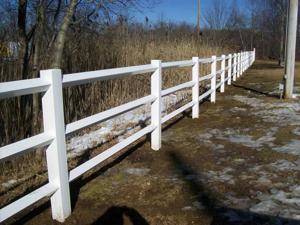 White wooden fence along a snowy path in a wooded rural area under a blue sky