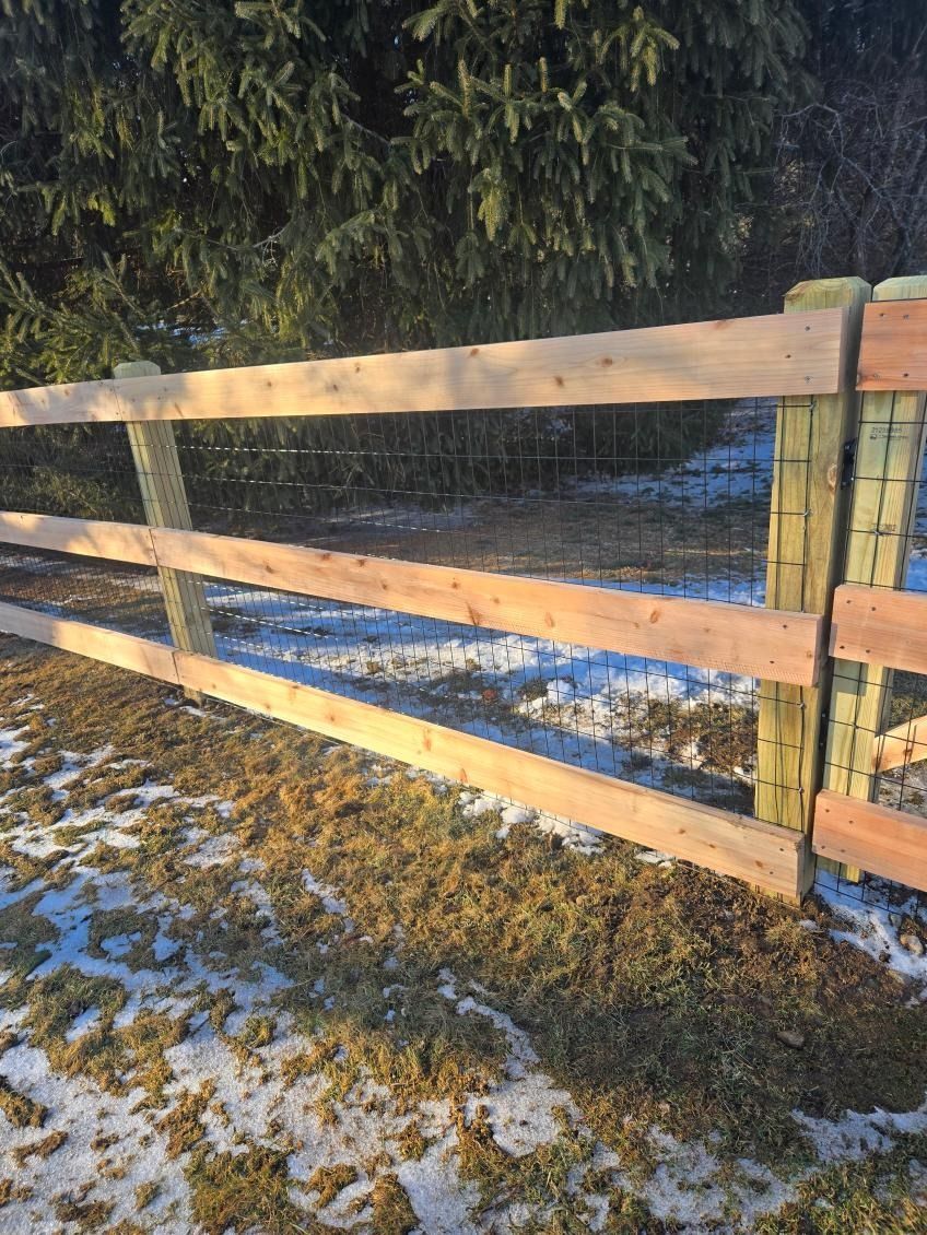 Wooden fence beside a snowy grassy field in winter sunlight
