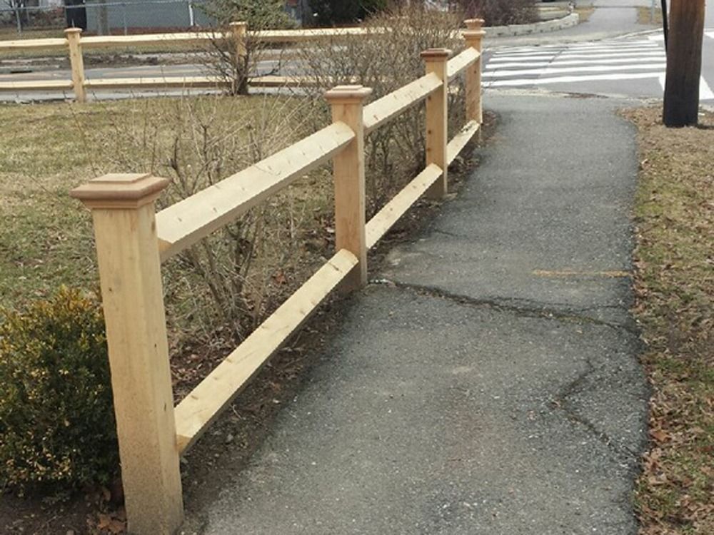Wooden fence lining a cracked sidewalk beside a road and crosswalk.