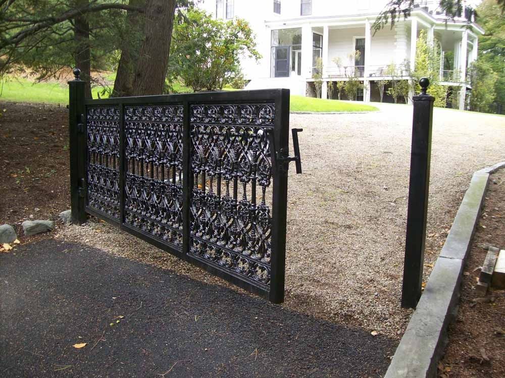 Black metal gate beside a gravel driveway in front of a white house