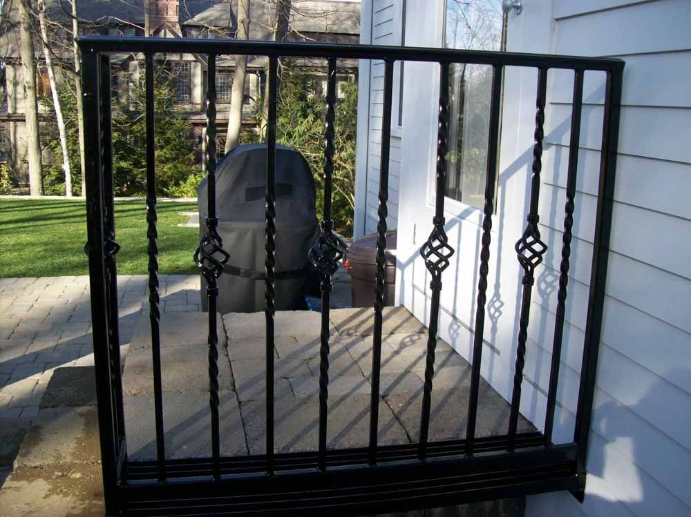 Black metal pet gate on a porch in front of a grill and white siding