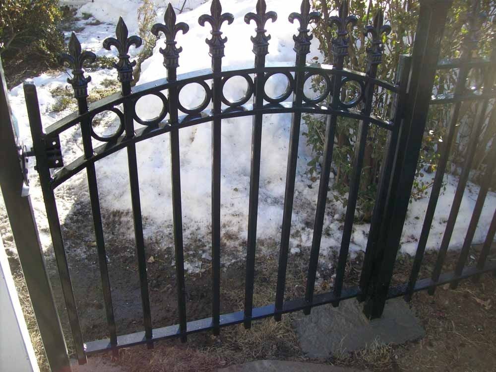 Black wrought-iron gate with pointed finials, partially open over a snowy or icy walkway.