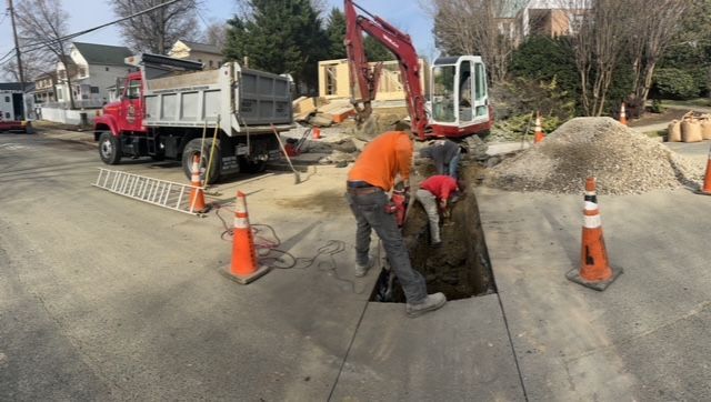 A group of construction workers are digging a hole in the sidewalk.