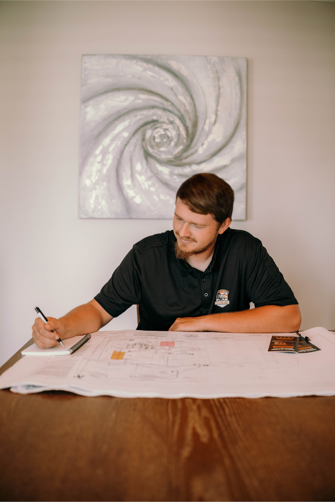 Man at table drawing on paper, artwork above, home interior.