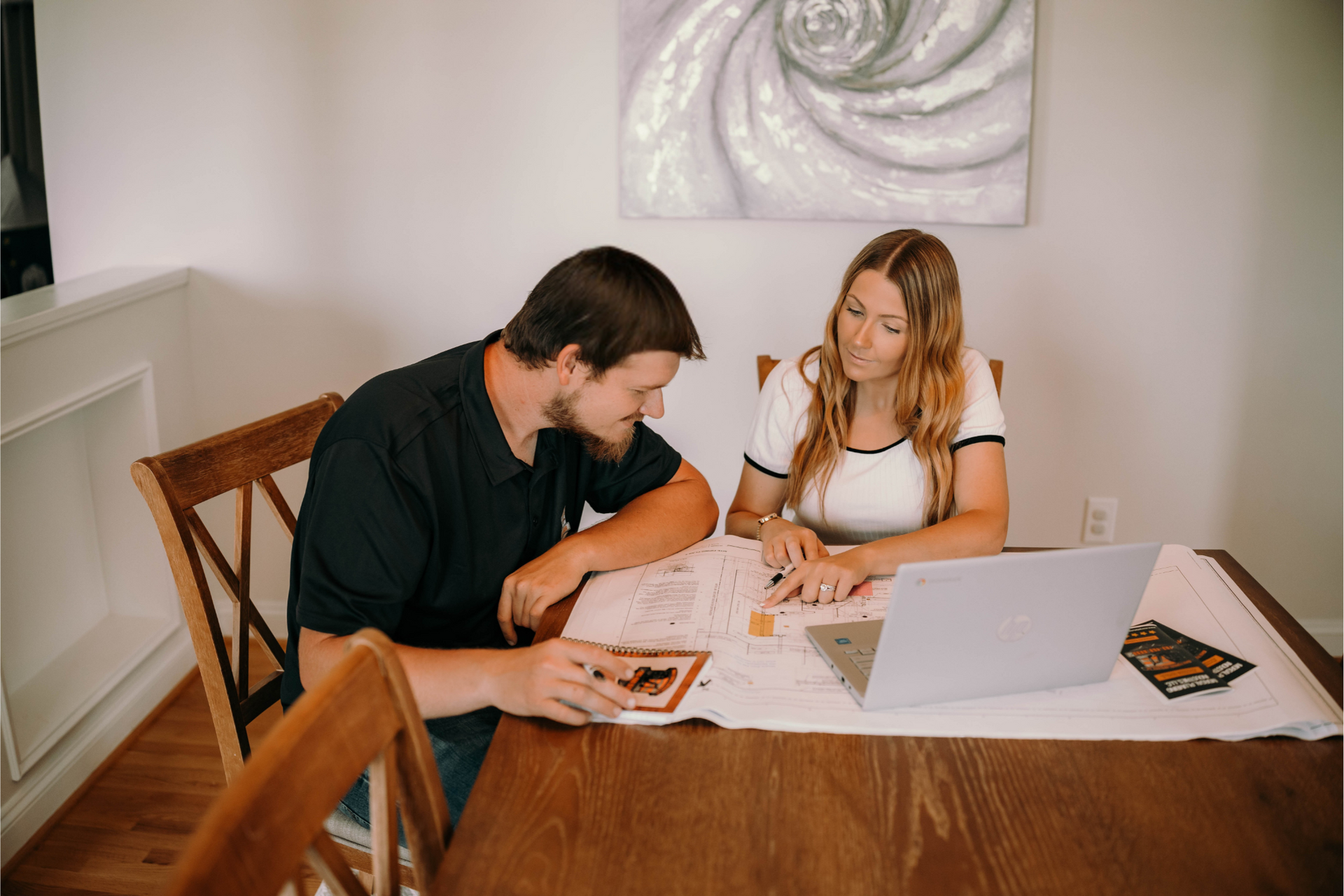 Couple reviewing documents at a dining table with laptop and a framed photo.