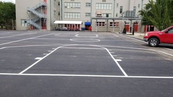 A red car is parked in a parking lot in front of a building