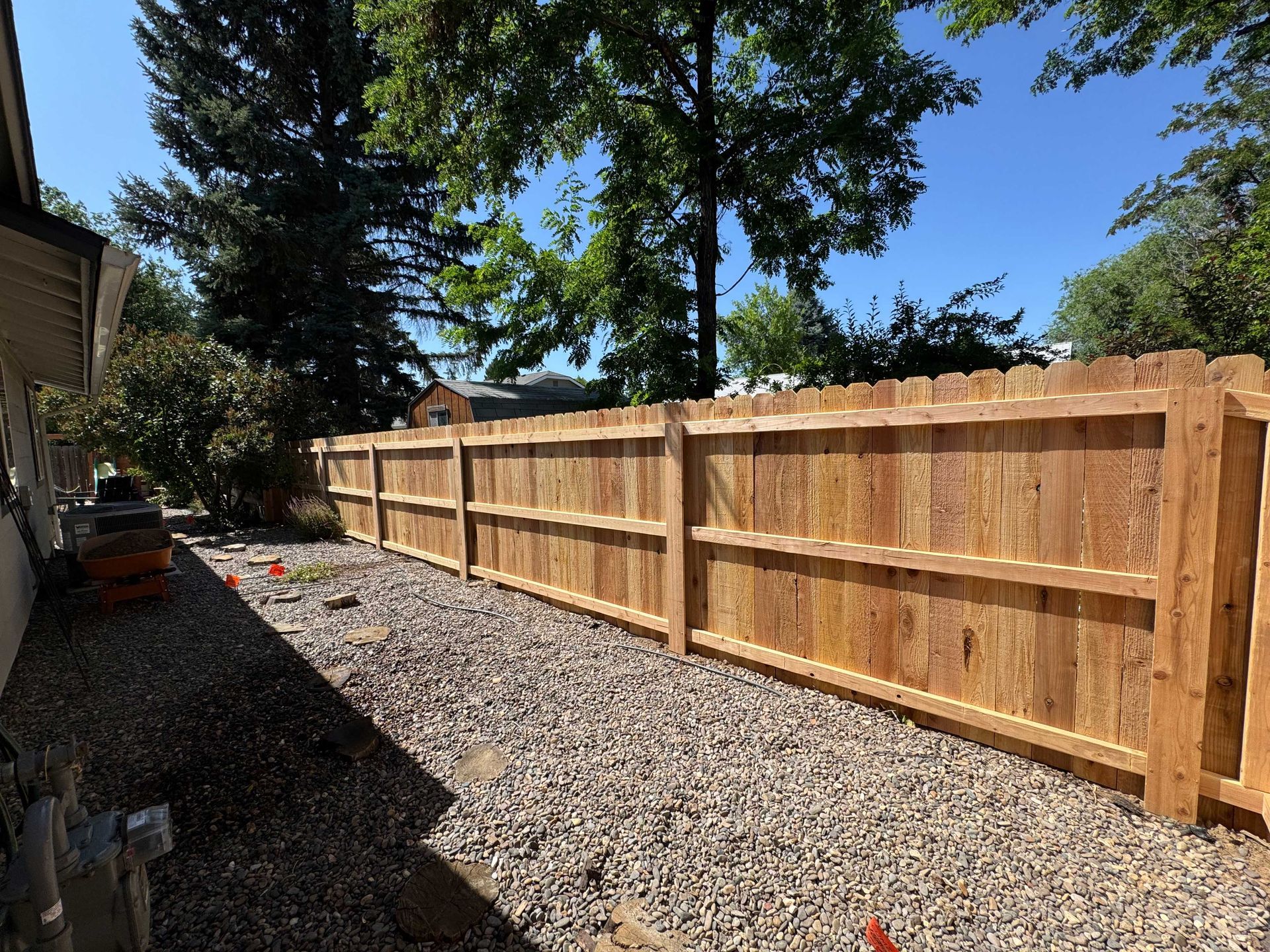 A newly built wood fence in a gravel-covered side yard with a sunny blue sky.