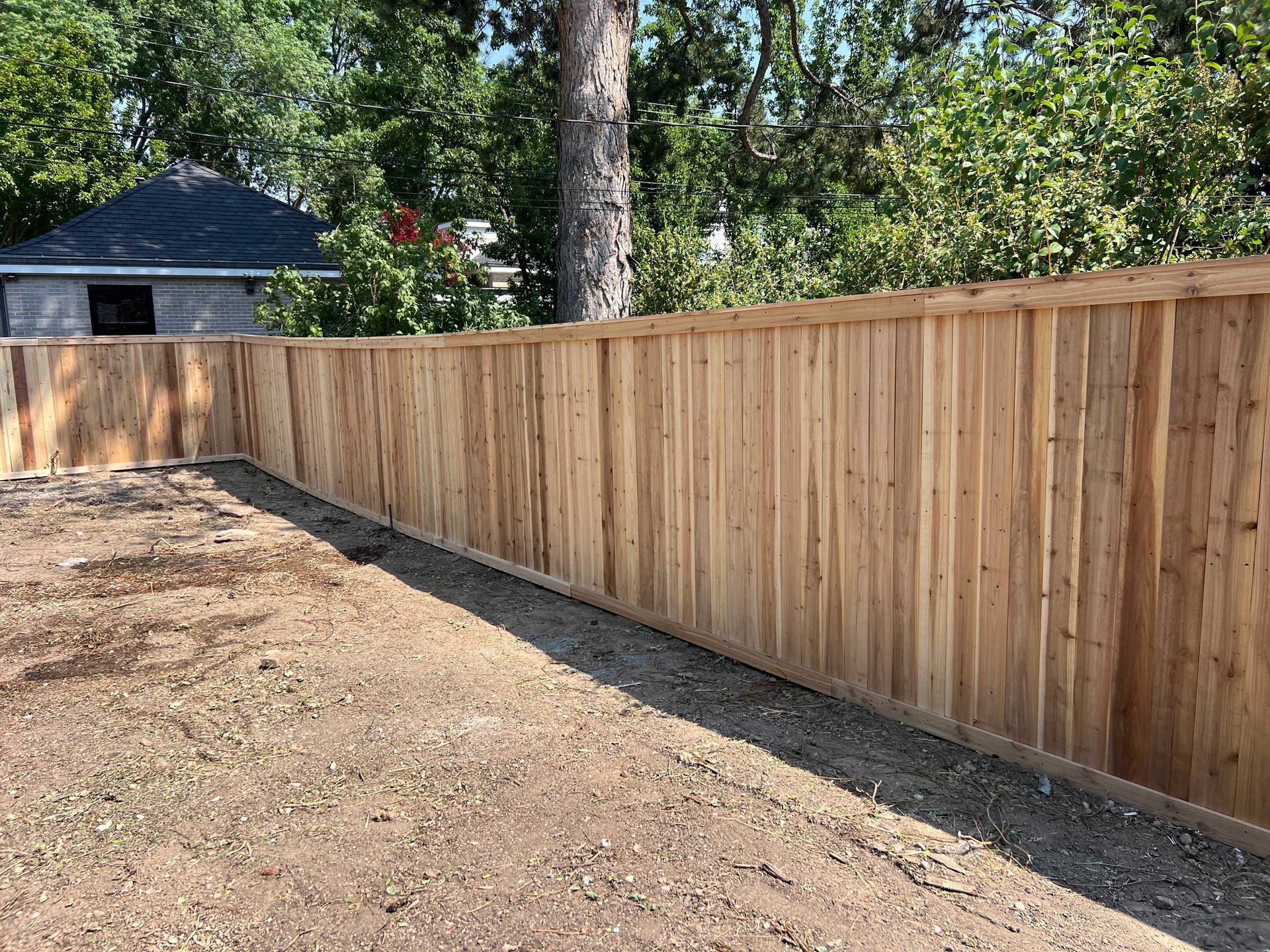 Wooden fence surrounding a gravel yard, with a building and trees in the background.