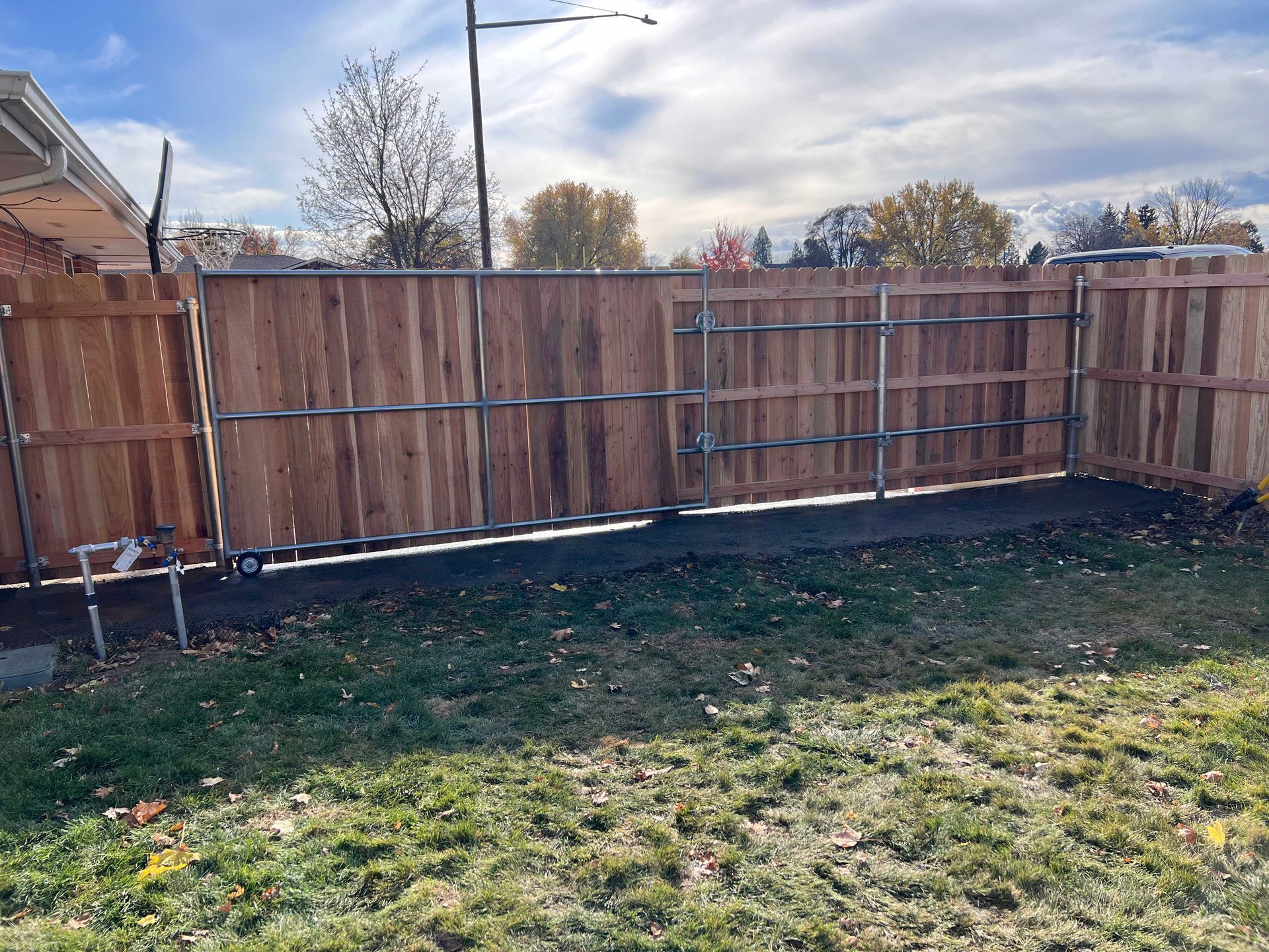 Wooden fence with metal supports and gate in a grassy backyard under a cloudy sky.