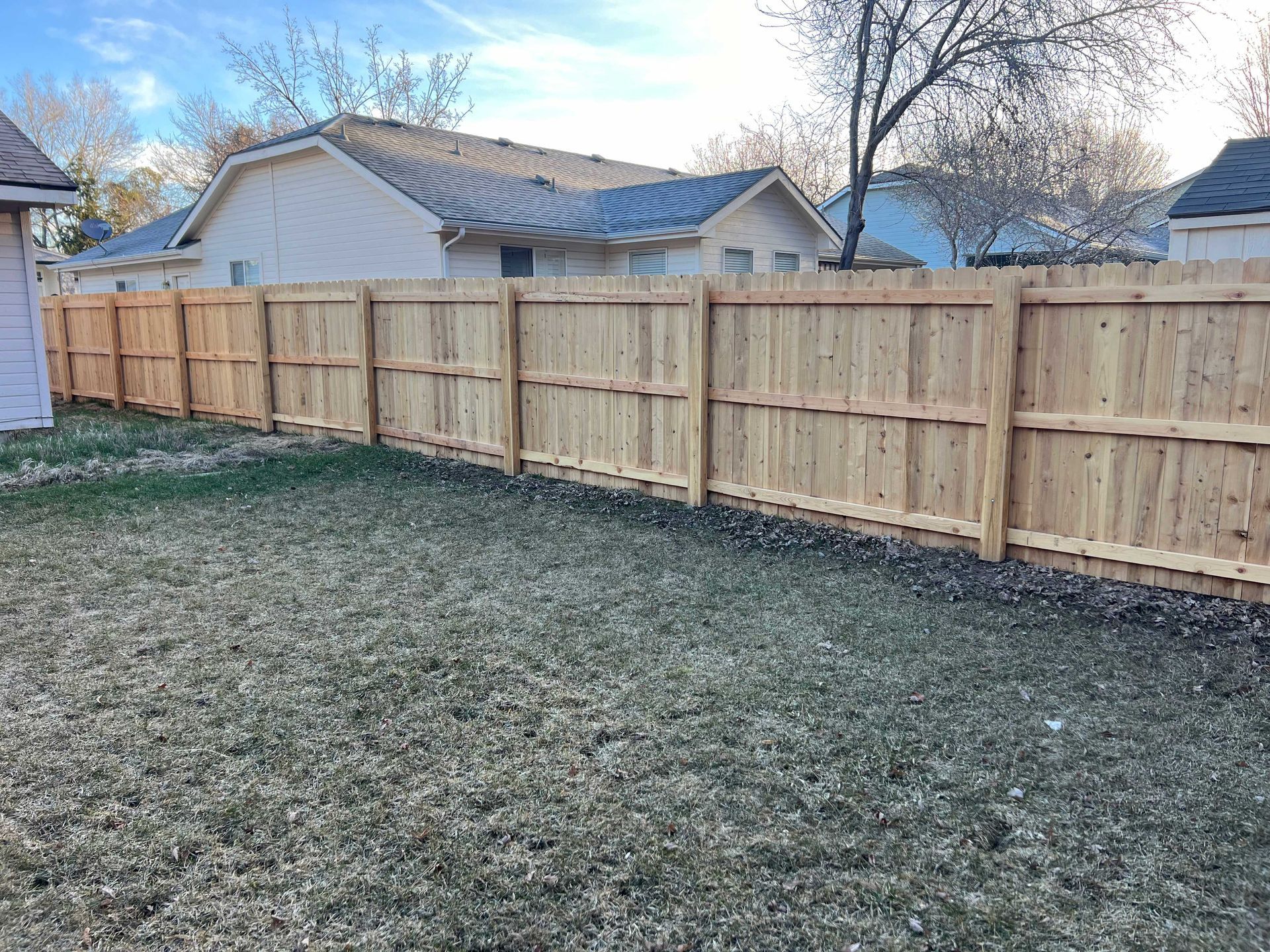 Wooden fence in a backyard, brown boards, green grass, blue sky background.