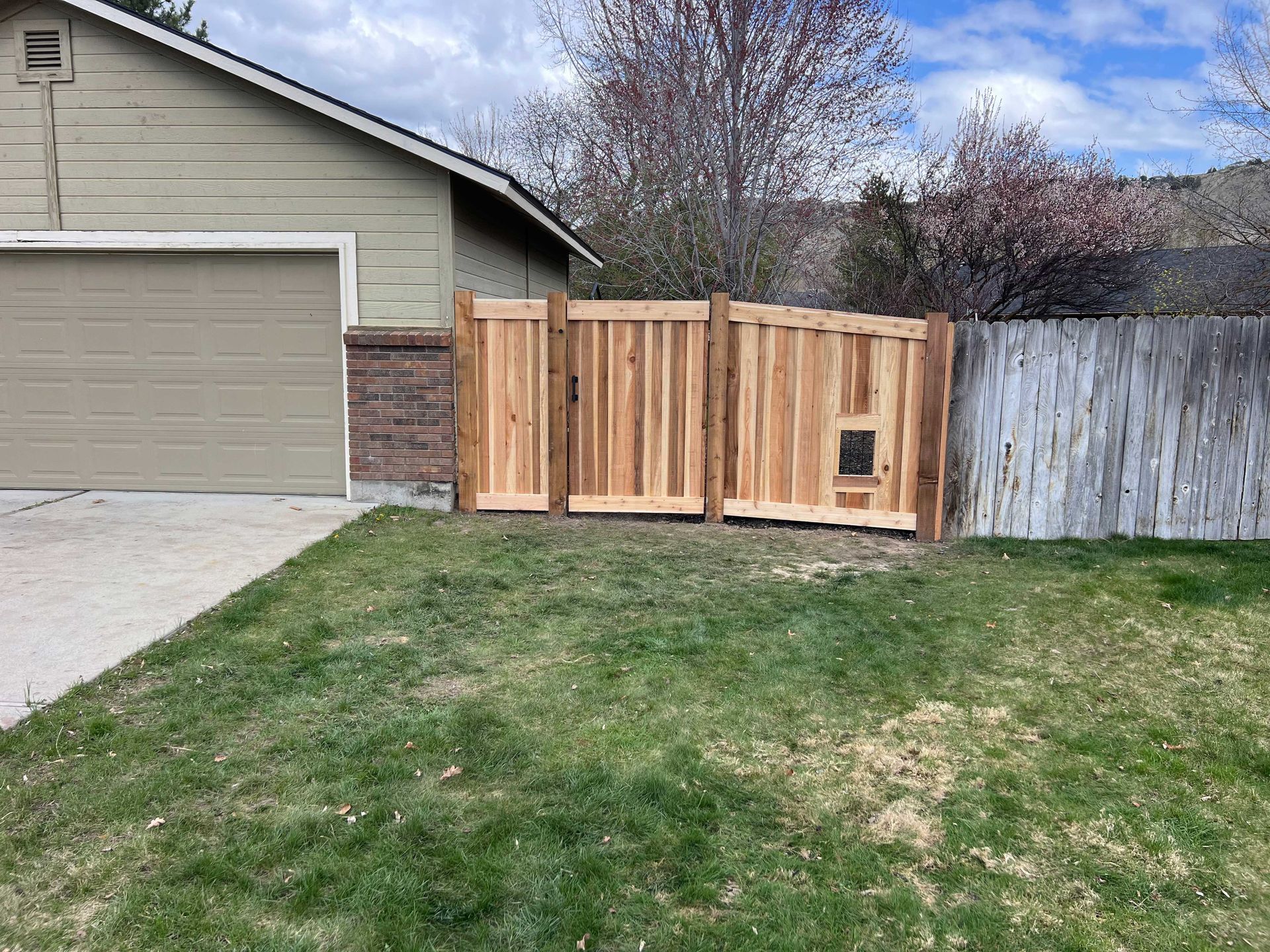 Wooden fence with dog door next to a garage and an existing fence.