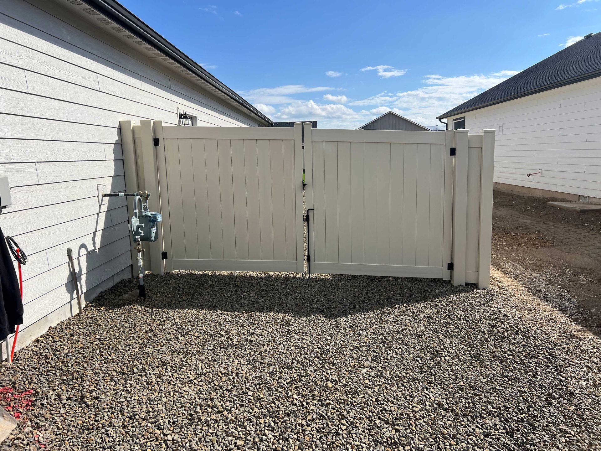 Cream-colored gate between two buildings, gravel ground. Blue sky.