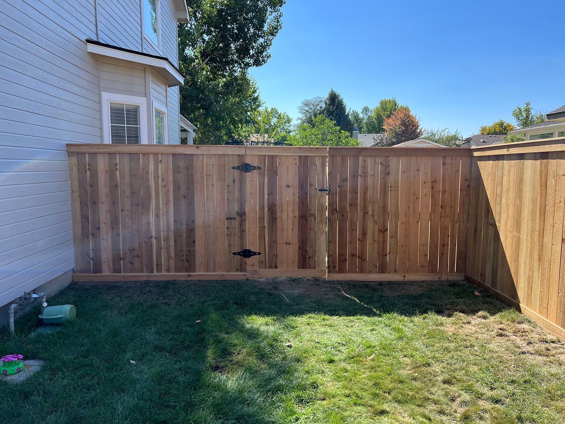 Wooden fence in a backyard with green grass under a clear blue sky.