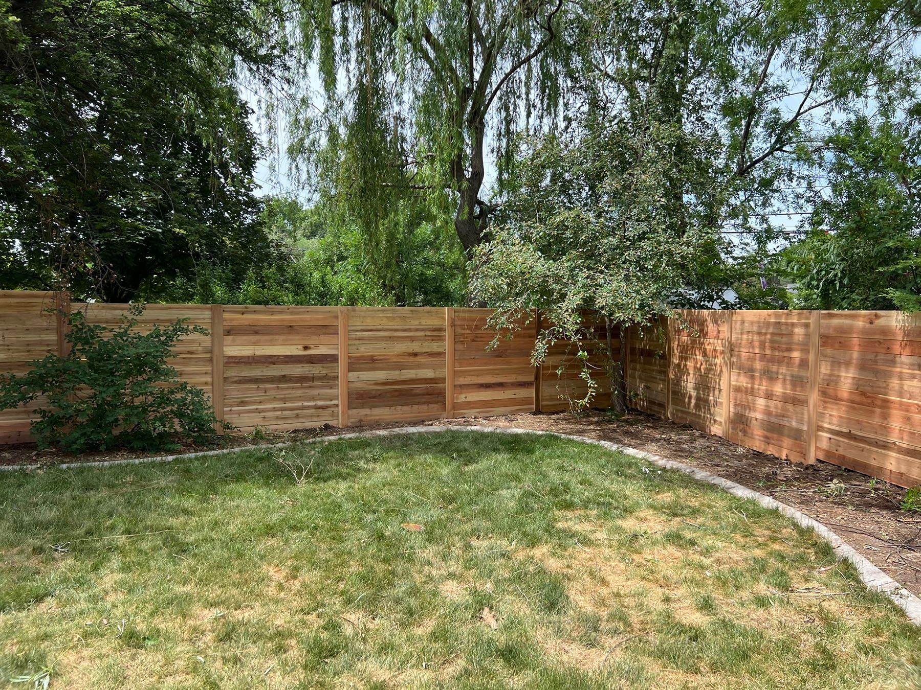 Backyard with wooden fence, green grass, and trees.