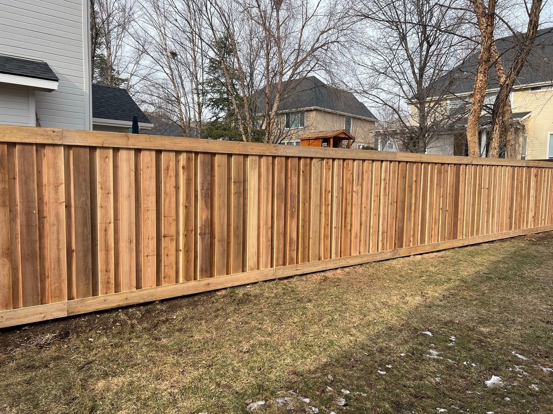 Wooden privacy fence in a grassy yard, houses in the background.