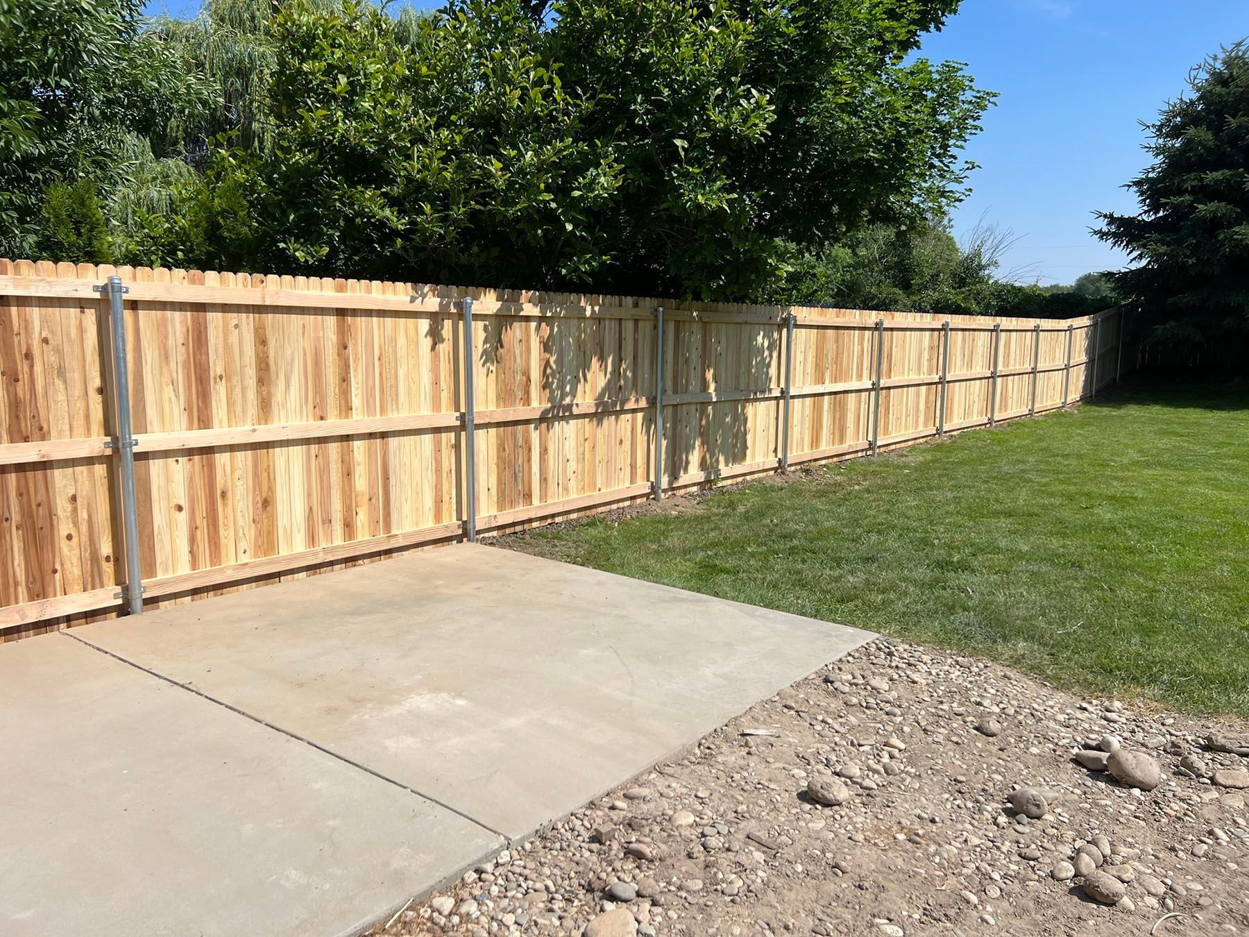 Wooden fence surrounding a grassy yard with a concrete patio.