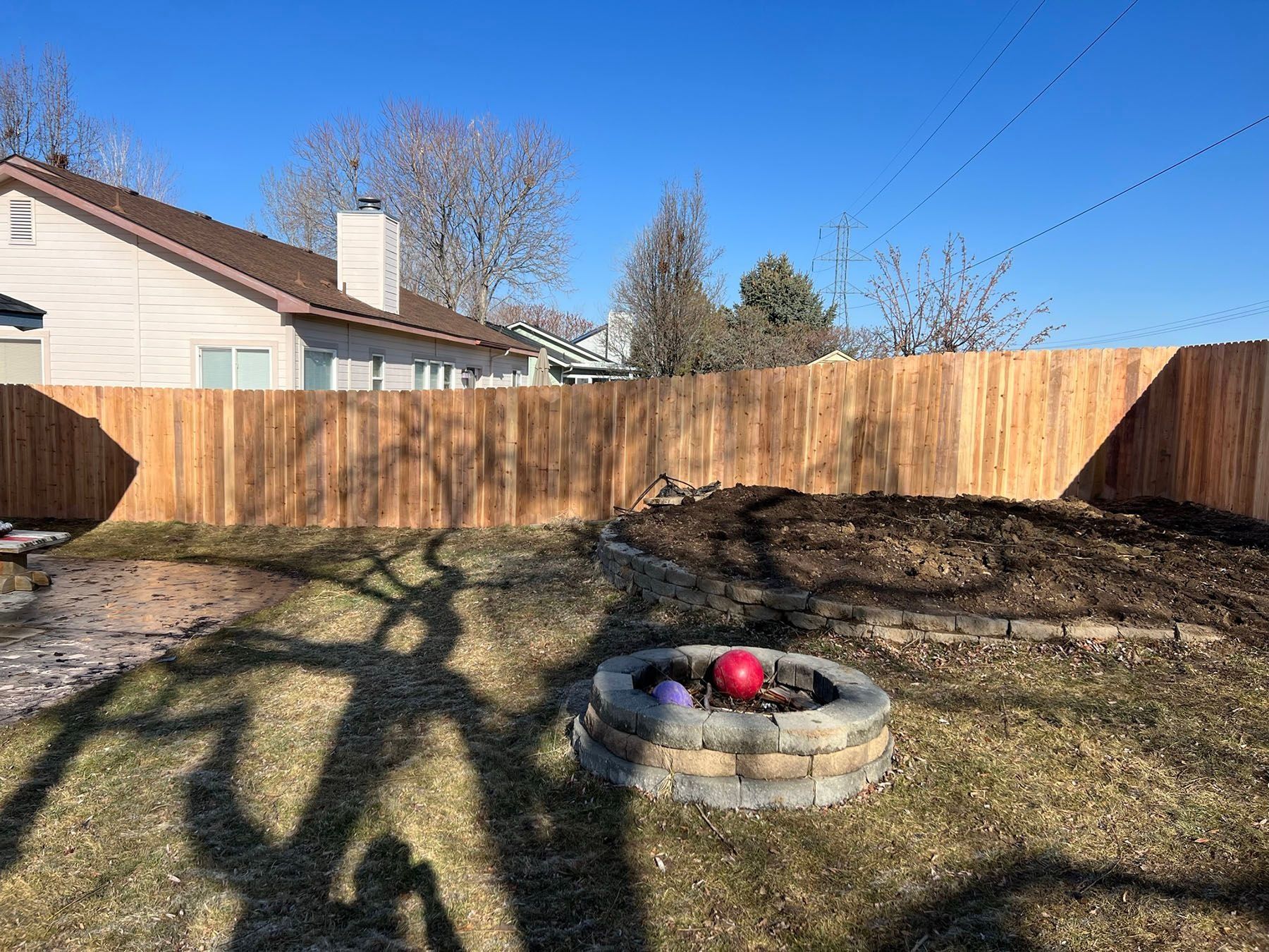 Backyard with a wooden fence, fire pit, and a house.