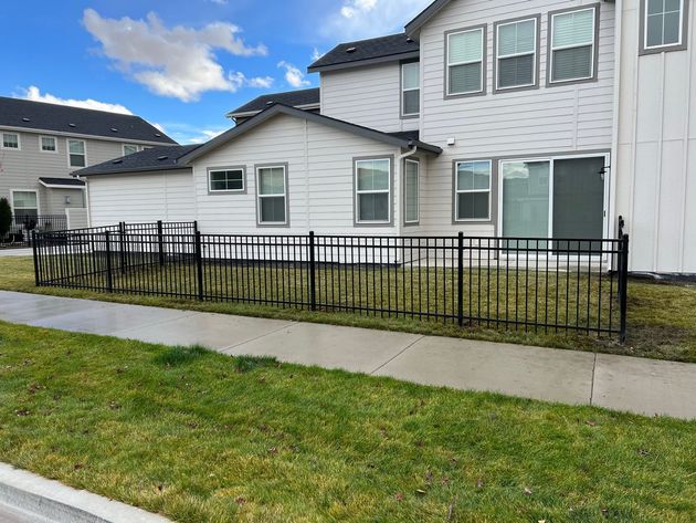 Black metal fence along a sidewalk, bordering a house with white siding and windows.