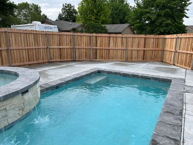 A backyard pool with a brown wooden fence, blue water, and gray stone edging.