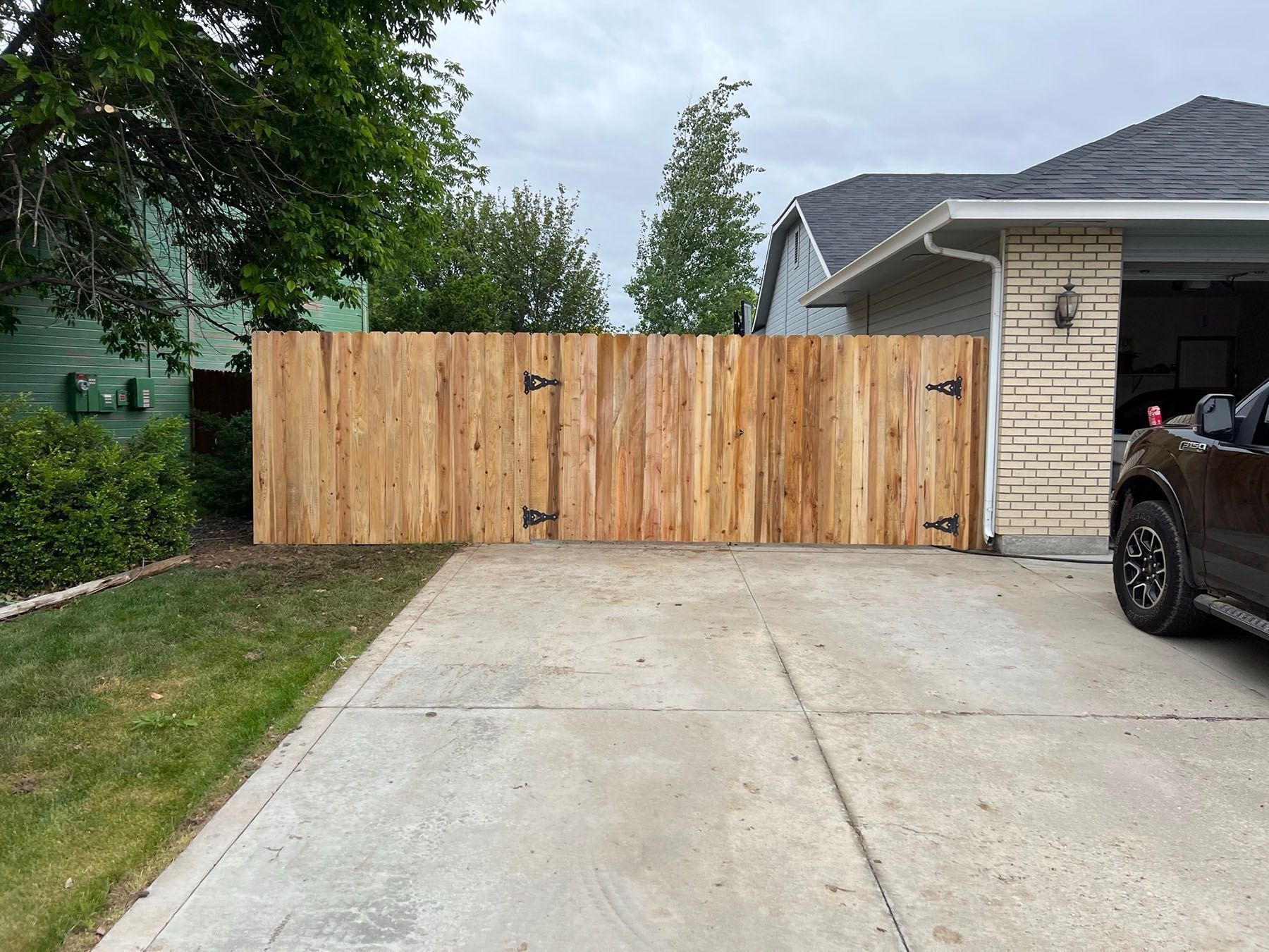Wooden fence across a driveway, attached to a garage. Overcast sky.
