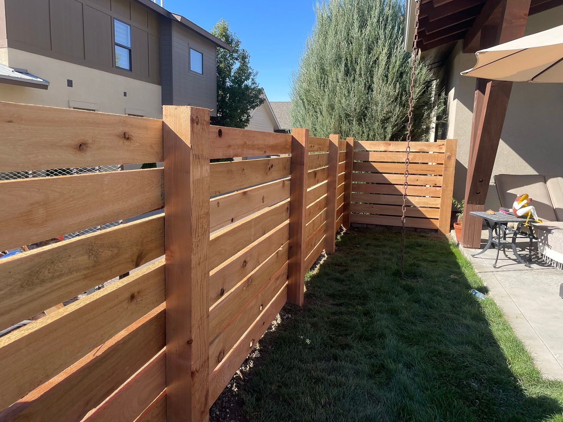 Wooden horizontal slat fence in a backyard, with green grass.