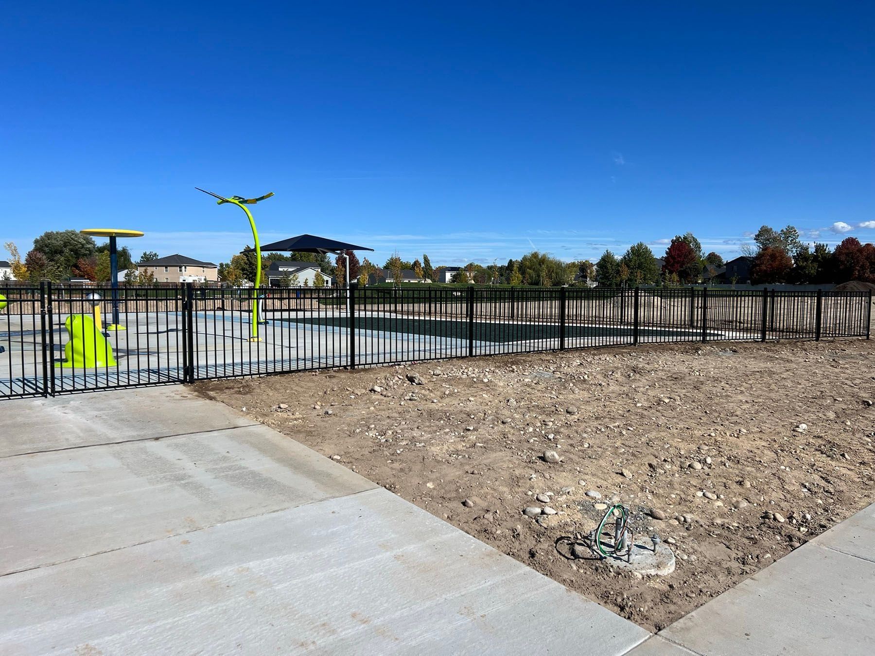 Playground with black fence, concrete path, and blue sky.