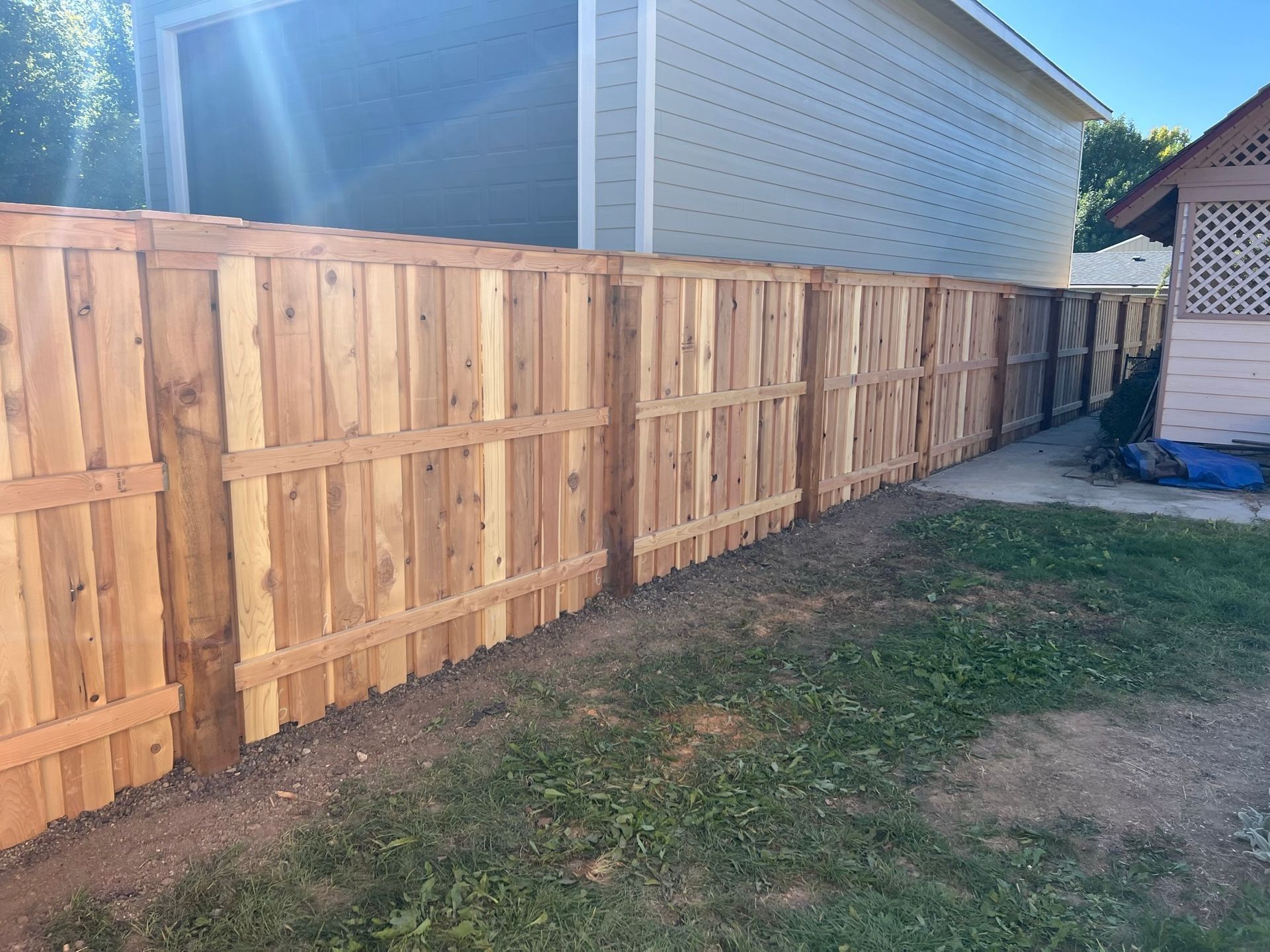 Wooden fence along a grassy area, in front of a light-colored building.