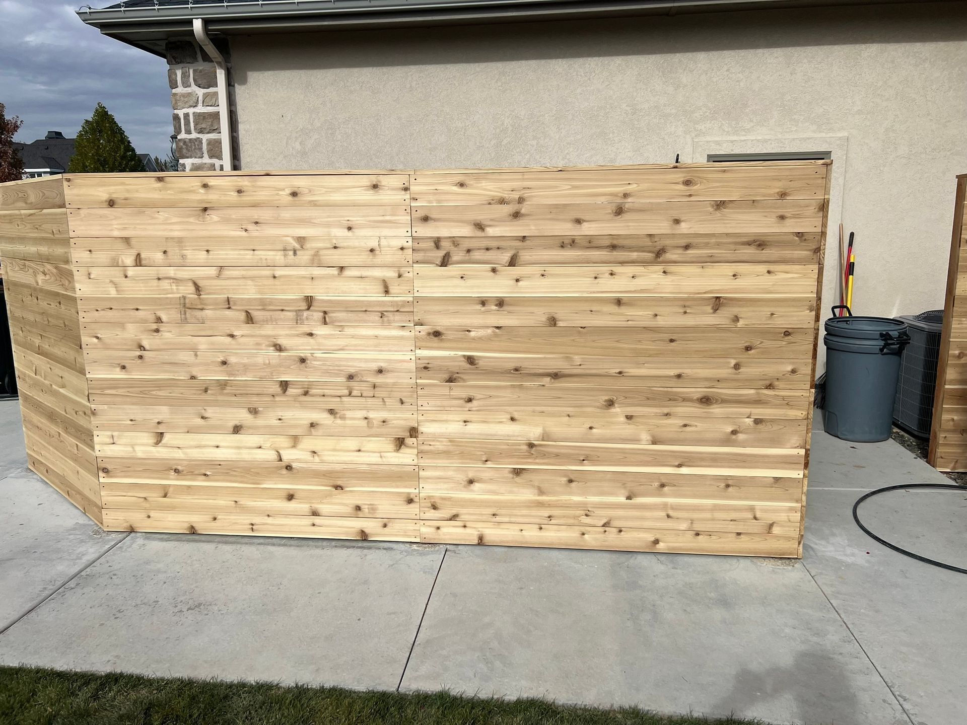 Wooden fence construction on a concrete patio beside a beige building.