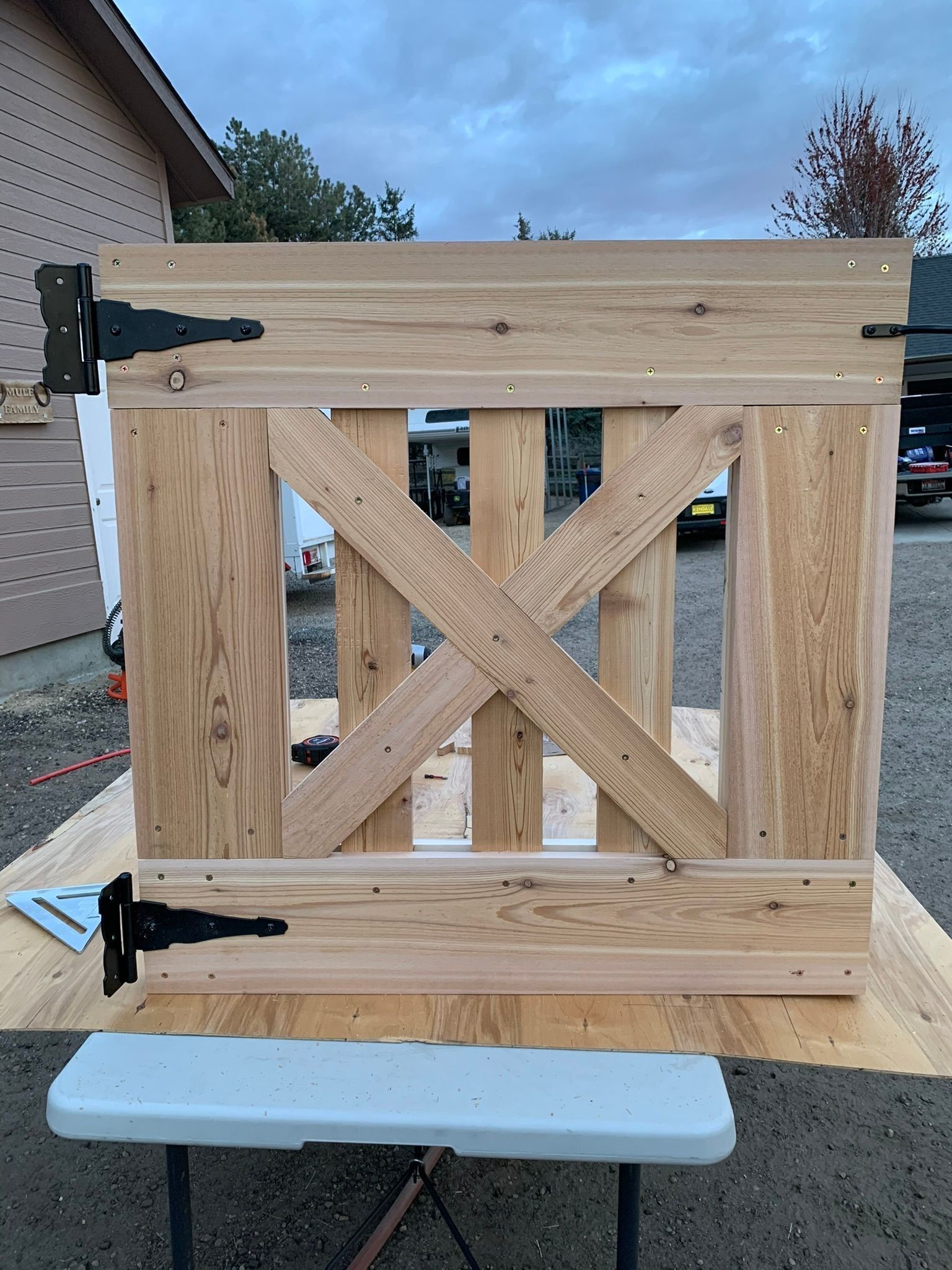 Wooden gate with an X-shaped design, black hinges, and a light-colored wood finish, resting on a table outdoors.