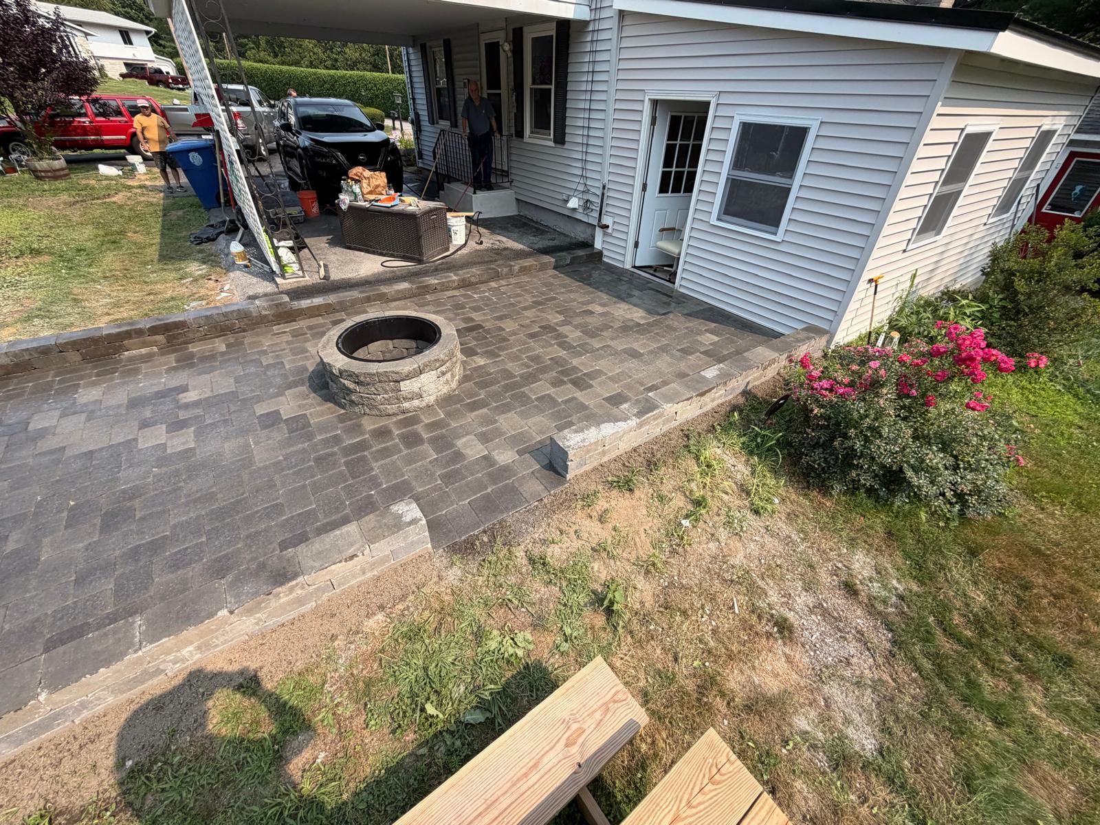 Backyard patio with brick pavers, a fire pit, covered carport, and a small white shed